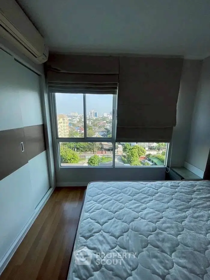 Cozy bedroom with large window offering stunning city view and ample natural light.