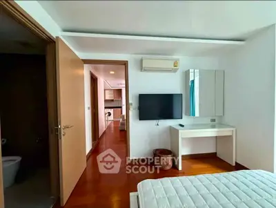 Modern bedroom with wooden flooring, wall-mounted TV, and air conditioning in a stylish apartment.