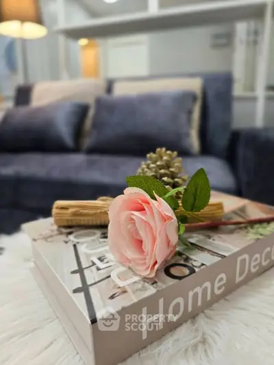 Elegant living room with plush sofa and stylish decor book featuring a pink rose, creating a cozy ambiance.