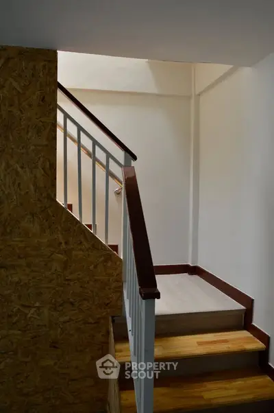 Modern staircase with wooden steps and sleek railing in a well-lit interior space.