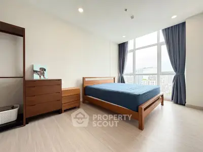 Spacious bedroom with large window and modern wooden furniture