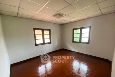Spacious empty room with wooden flooring and large windows, perfect for customization.