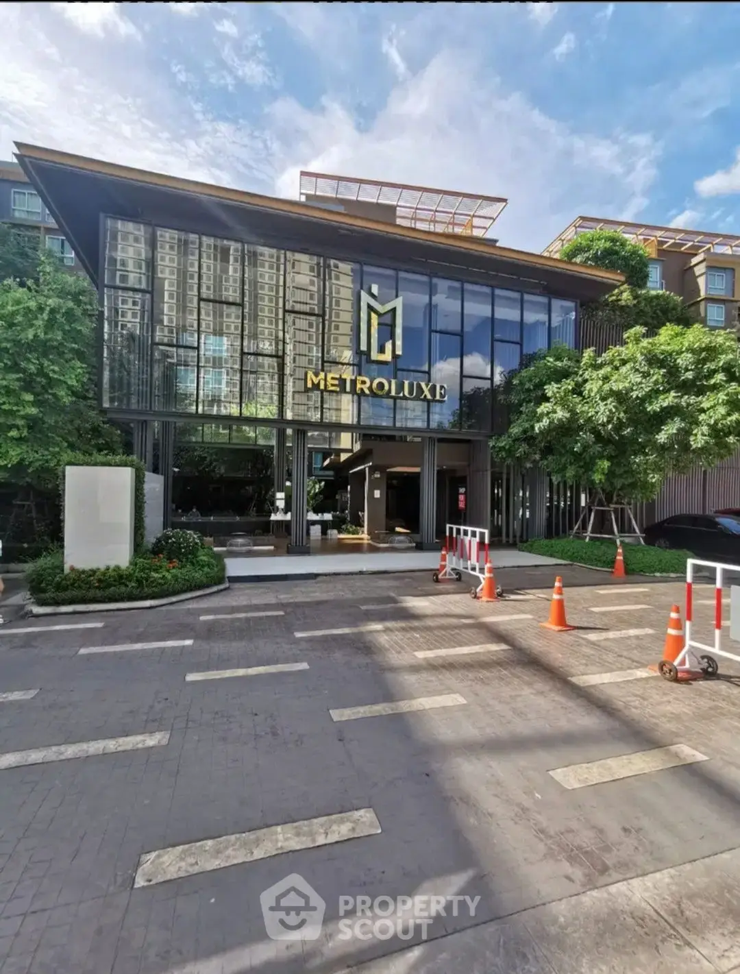 Modern building entrance with glass facade and lush greenery, ideal for urban living.