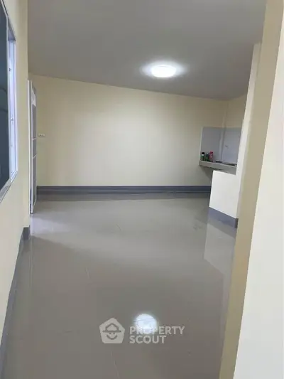 Spacious empty room with tiled flooring and small kitchen area