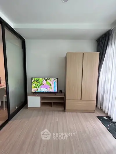 Modern living room with sleek wooden flooring, TV unit, and wardrobe, featuring a large window for natural light.