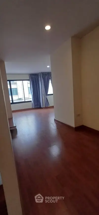 Spacious empty room with wooden flooring and large window, ideal for customization.