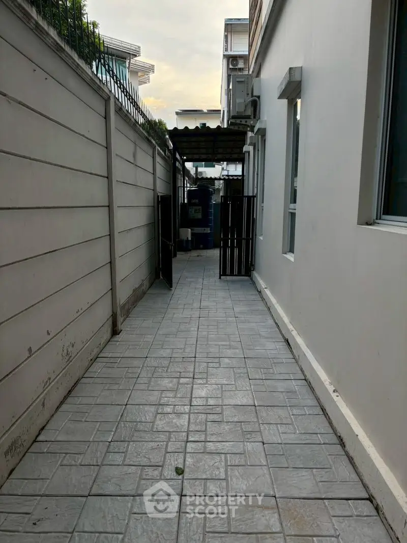 Narrow exterior walkway beside modern building with tiled pathway and gate.