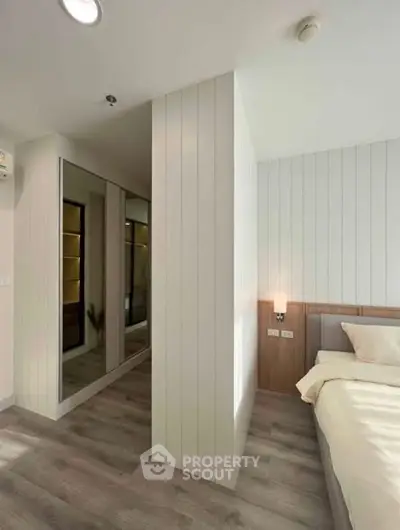 Modern bedroom with sleek design and mirrored closet doors, featuring elegant lighting and wood panel accents.
