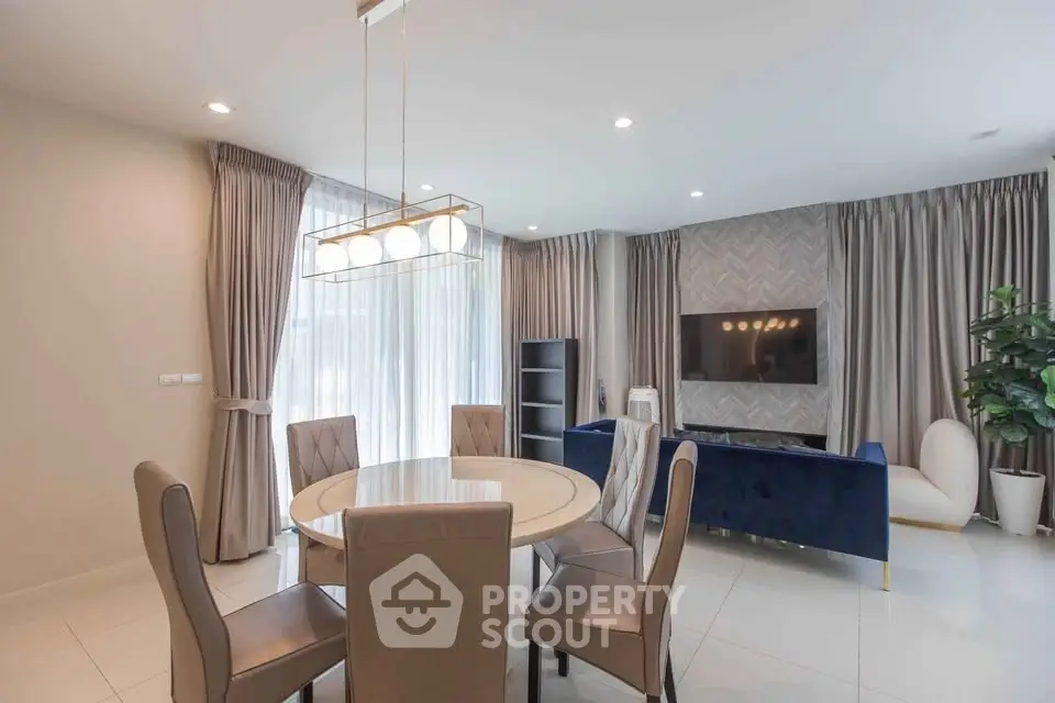 Elegant dining area with modern round table and stylish chairs, featuring a cozy living space with a TV and lush curtains.