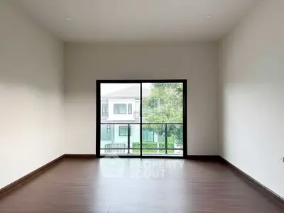 Spacious empty room with large window offering a view of modern residential buildings.