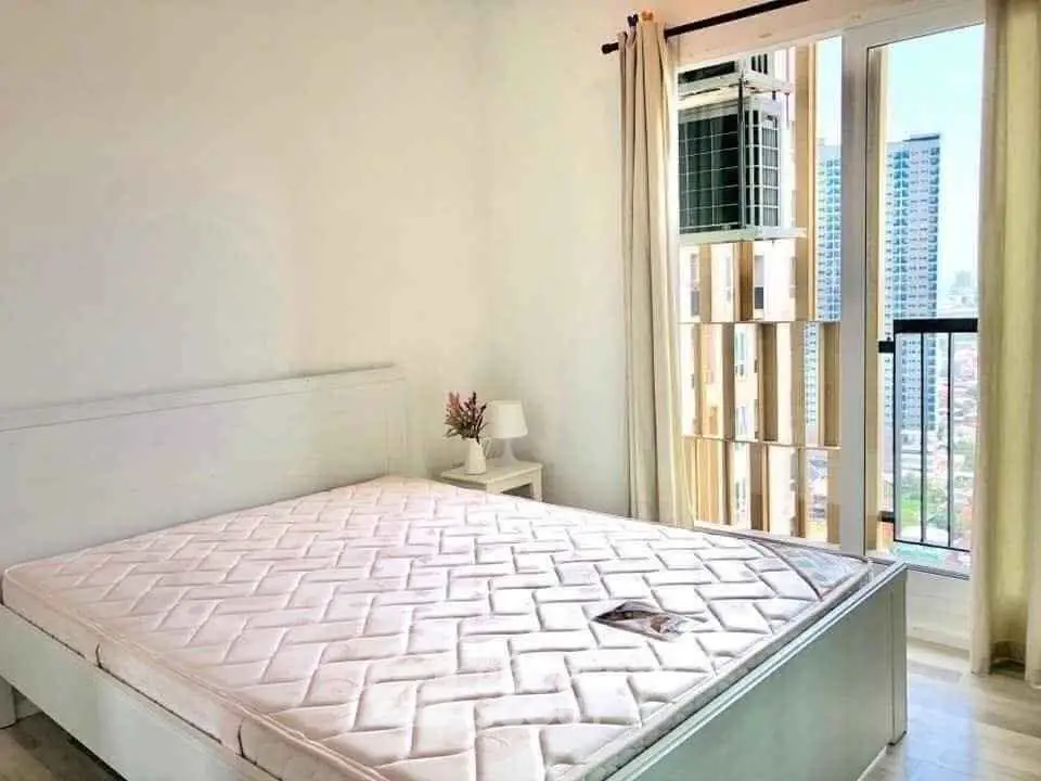 Bright bedroom with city view and large window, featuring a comfortable bed and modern decor.