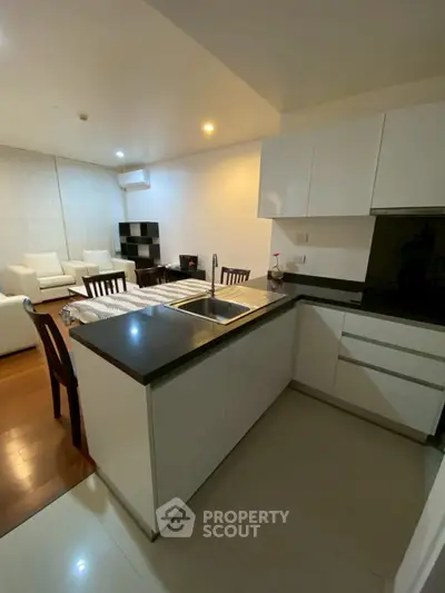 Modern open-layout kitchen with sleek cabinetry and cozy living room area in a stylish apartment.