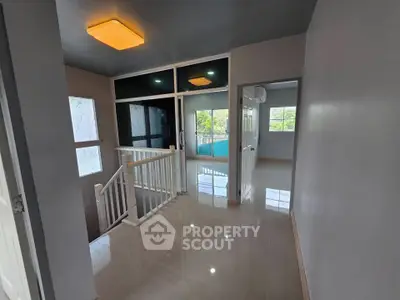 Spacious hallway with modern lighting and glossy tiled flooring, leading to a bright room with large windows.