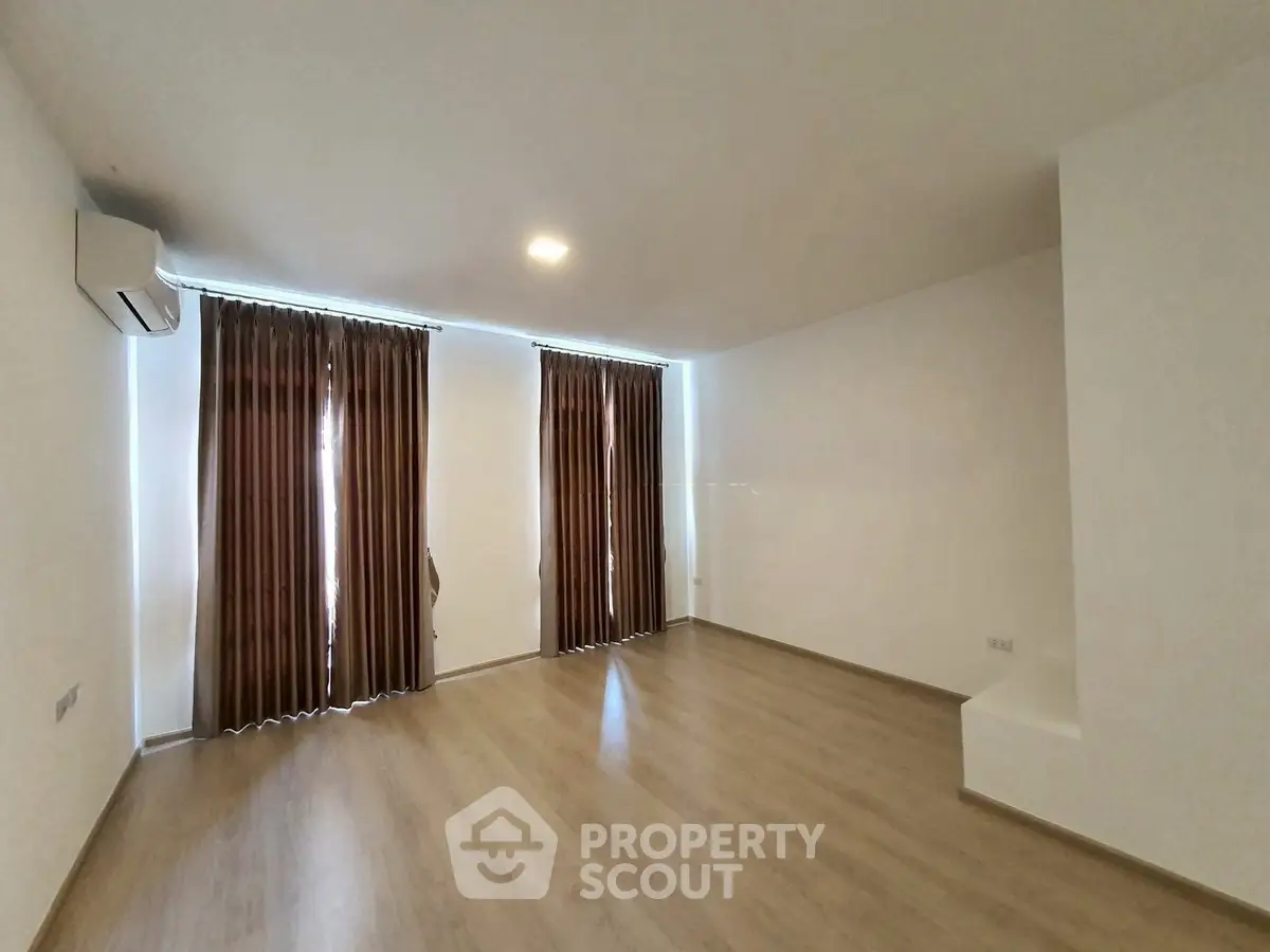 Spacious empty room with wooden flooring and large windows, perfect for customization.