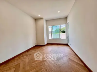 Spacious empty room with wooden herringbone flooring and large window