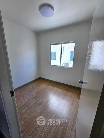 Spacious empty bedroom with wooden flooring and natural light from window.