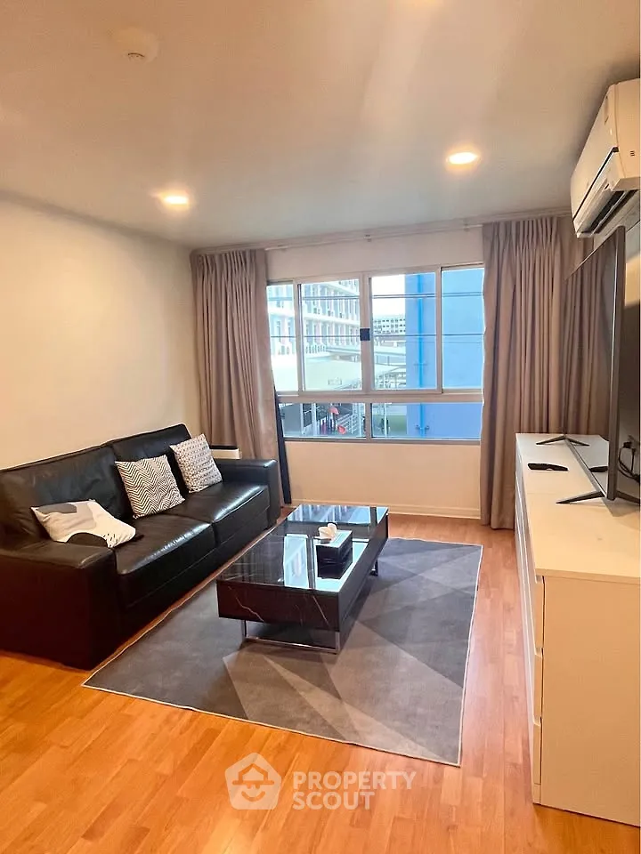 Modern living room with sleek furniture and large window offering city views.