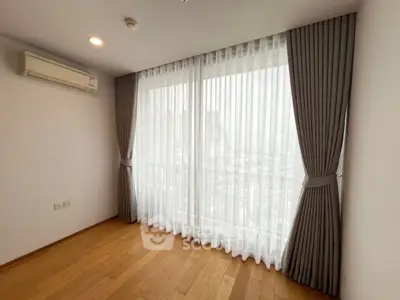 Spacious room with large window and elegant curtains, featuring wooden flooring and air conditioning.