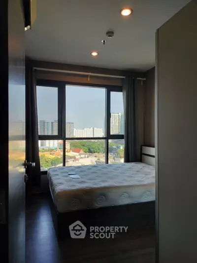 Modern bedroom with large window offering stunning city view in high-rise apartment.