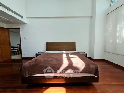 Spacious bedroom with wooden flooring and modern bed in natural light.