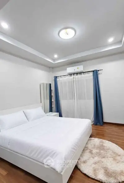 Modern bedroom with cozy white bed, wooden flooring, and elegant blue curtains.