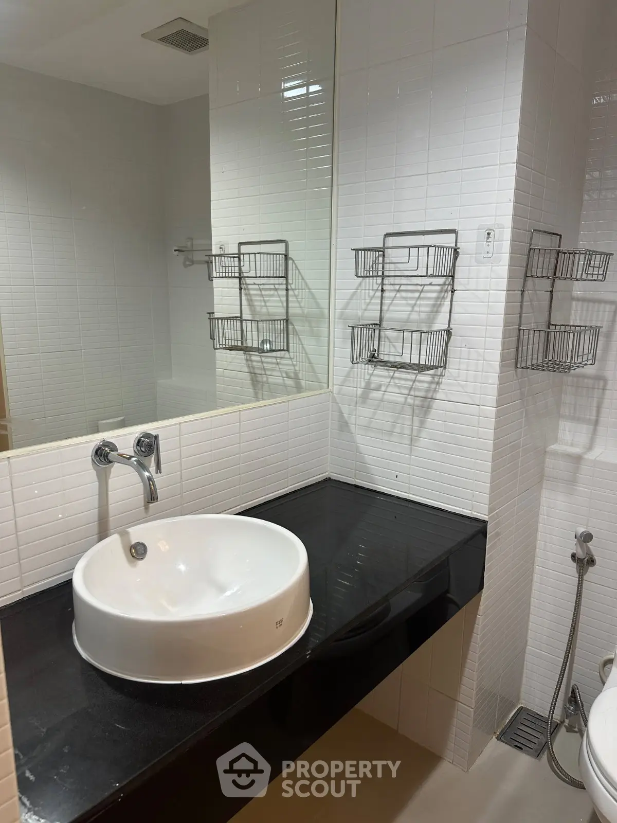 Modern bathroom with sleek black countertop and white basin, featuring wall-mounted storage baskets.