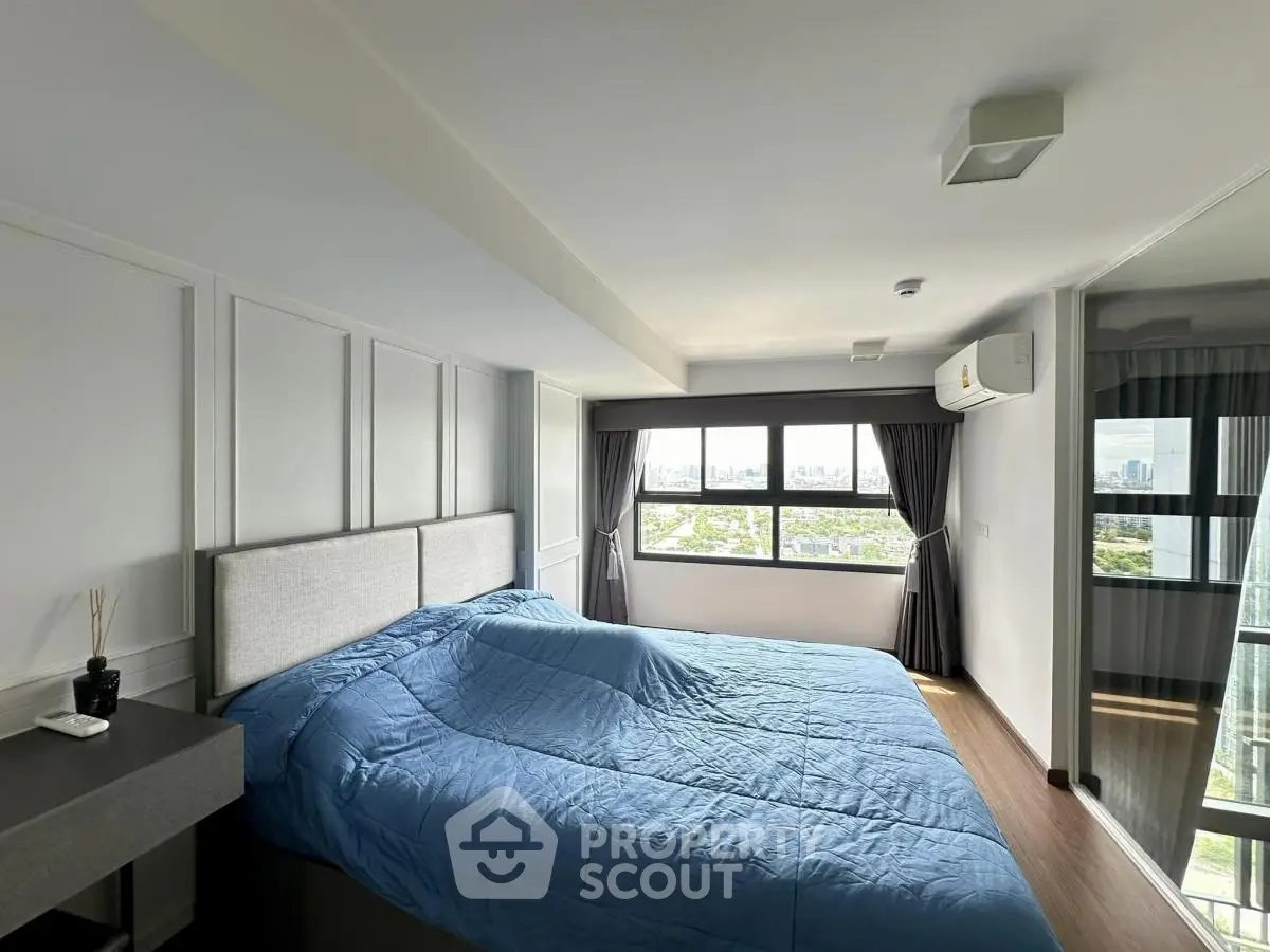 Spacious bedroom with large windows offering a stunning city view, modern decor, and ample natural light.