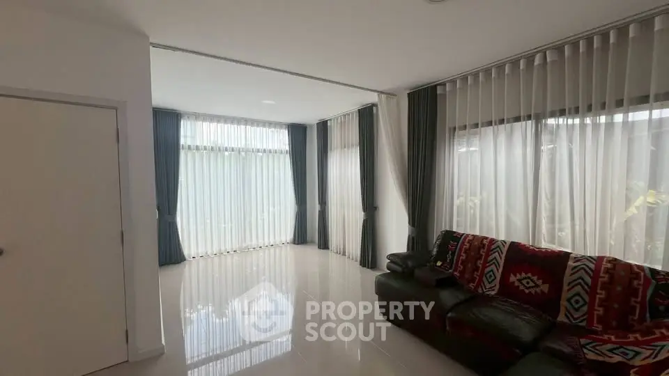 Spacious living room with large windows and elegant curtains, featuring a cozy sofa and sleek flooring.