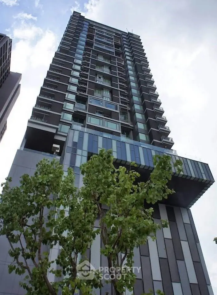 Modern high-rise building with sleek architecture and lush greenery in urban setting.