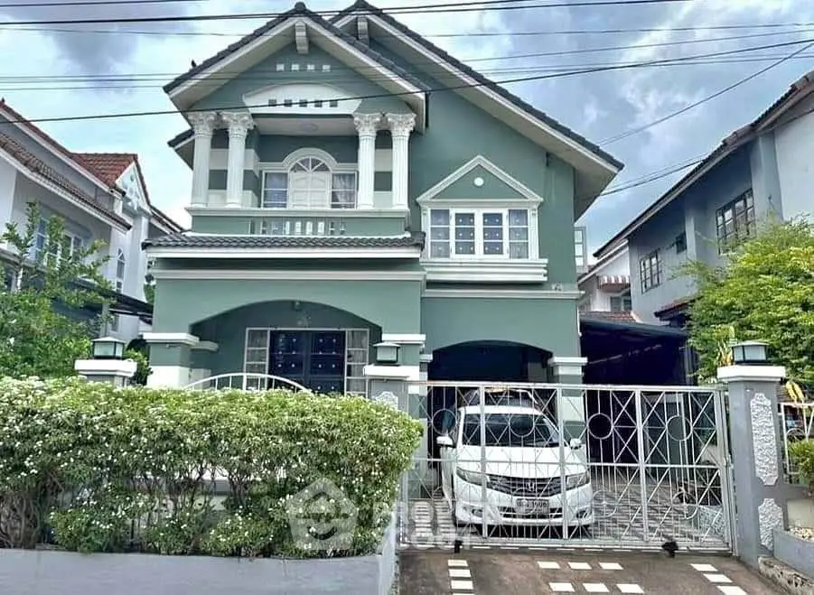 Charming two-story green house with gated driveway and lush garden, perfect for family living.