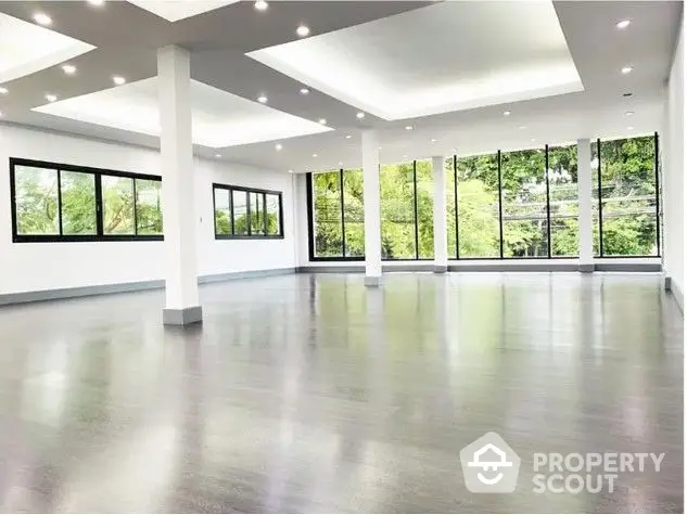 Spacious and modern living area with gleaming floors, abundant natural light from floor-to-ceiling windows, and a serene view of lush greenery.