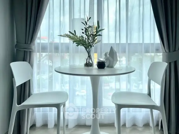 Chic modern dining nook with elegant white chairs and table by a sunlit window.