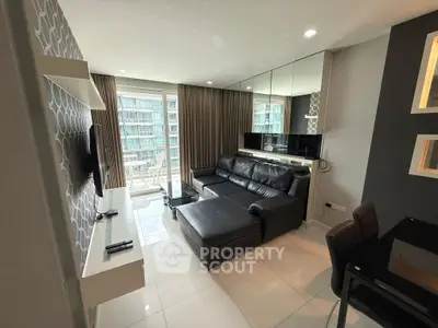 Modern living room with sleek black leather sofa and large TV, featuring floor-to-ceiling windows.