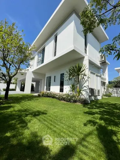 Modern white two-story house with lush green lawn and trees