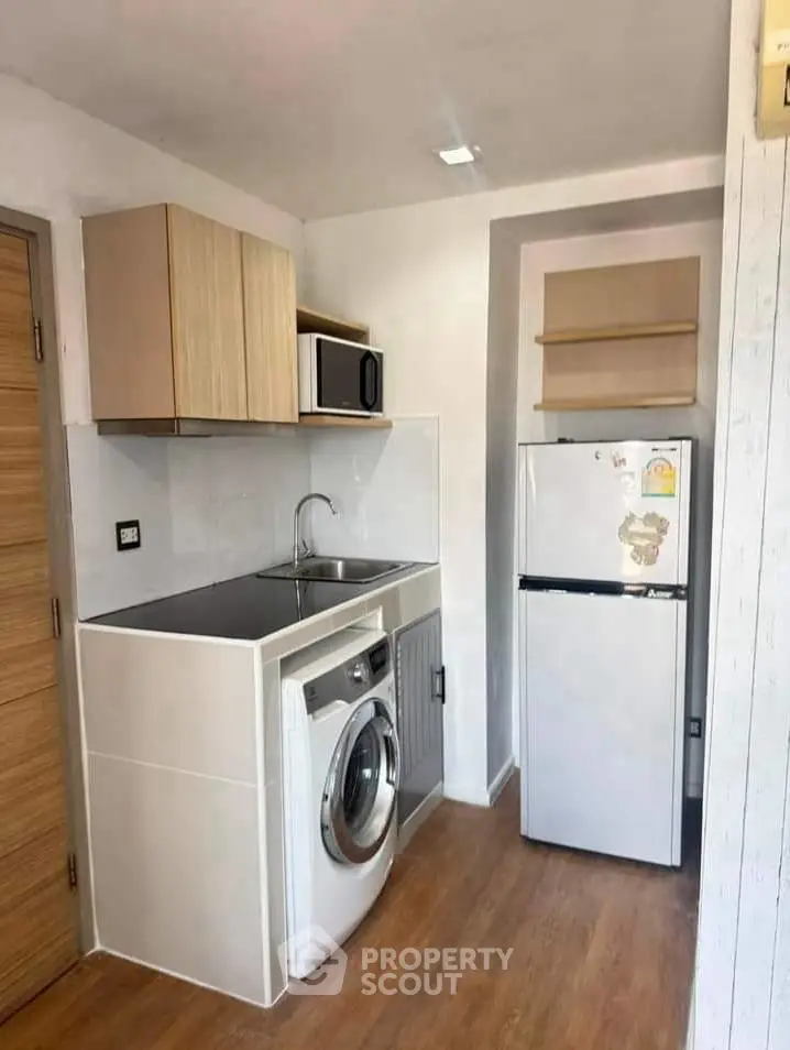 Compact kitchen with washing machine, fridge, and microwave in modern apartment.