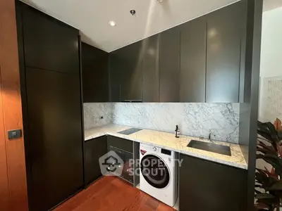 Modern kitchen with sleek black cabinets, marble countertops, and built-in appliances including a washing machine.