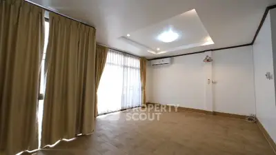 Spacious empty room with wooden flooring and large windows with curtains
