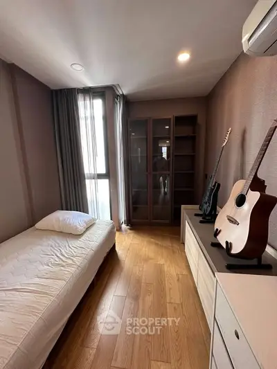 Cozy bedroom with wooden floor, single bed, and guitar display, perfect for music lovers.