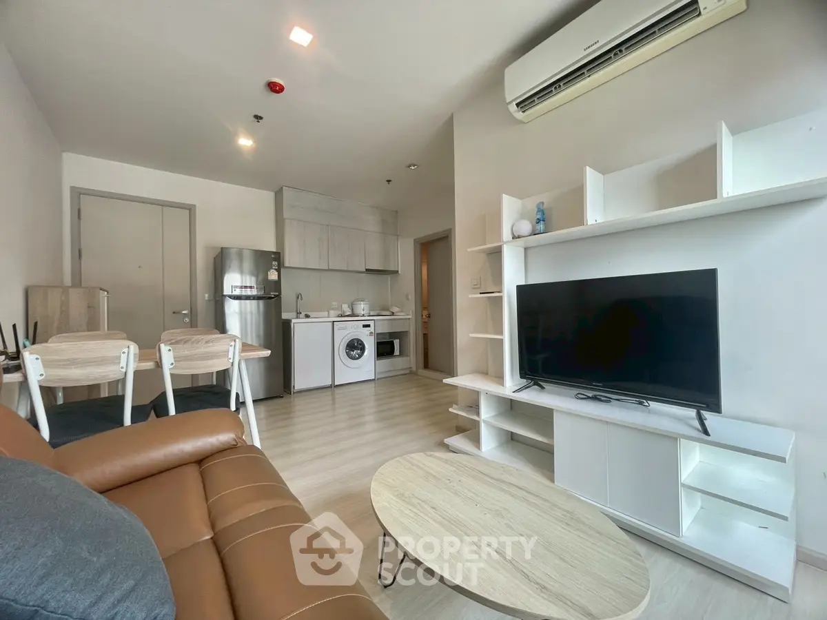 Modern living room with open kitchen, featuring sleek furniture and appliances in a cozy apartment setting.