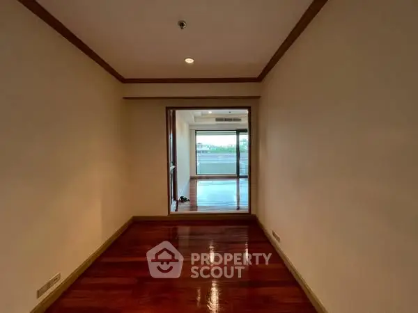 Spacious hallway leading to a bright room with large windows and wooden flooring.