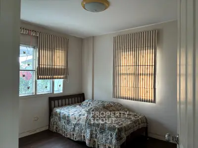 Cozy bedroom with natural light and wooden flooring, featuring a comfortable bed and striped window blinds.