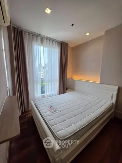 Cozy bedroom with large window and city view, featuring a comfortable bed and elegant curtains.
