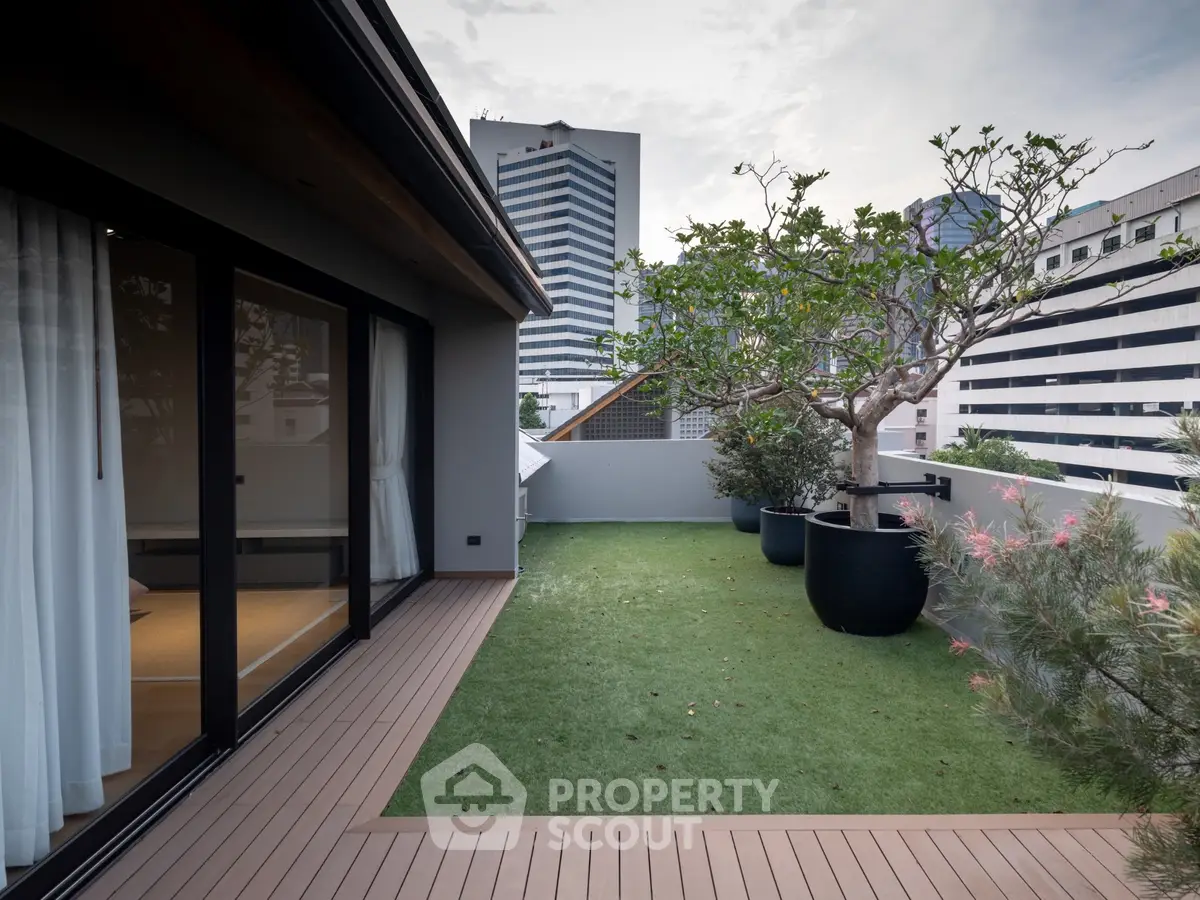 Luxurious rooftop garden with city view, featuring elegant wooden decking and lush greenery.