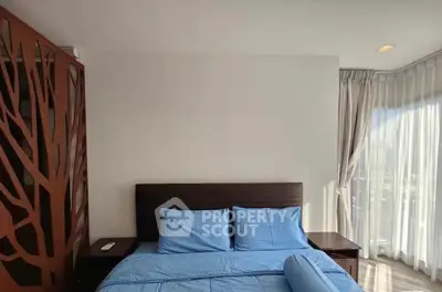 Modern bedroom with blue bedding and natural light from large windows.