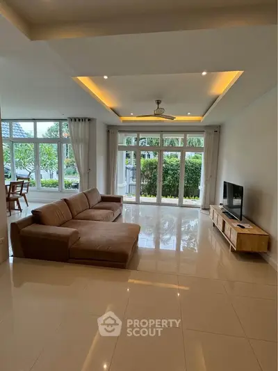 Spacious living room with modern sofa and large windows overlooking garden.