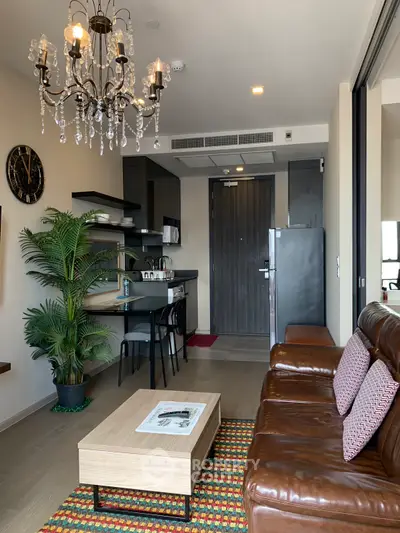Stylish modern living room with leather sofa, chandelier, and open kitchen layout in a cozy apartment.