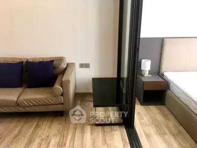 Modern studio apartment with cozy living area and stylish bedroom separated by glass partition.