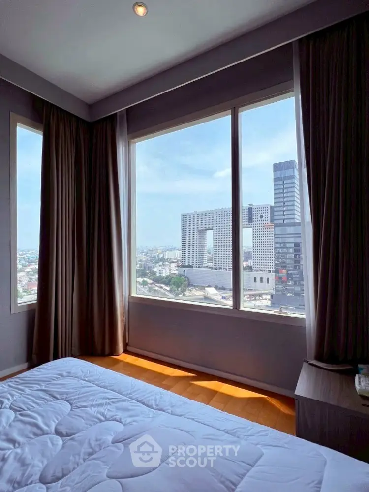 Spacious bedroom with stunning city view through large windows, offering natural light and modern urban living.