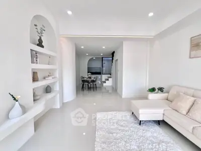 Modern living room with sleek white decor and open layout, featuring elegant built-in shelves and cozy seating area.