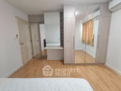 Spacious bedroom with mirrored wardrobe and wooden flooring in modern apartment.